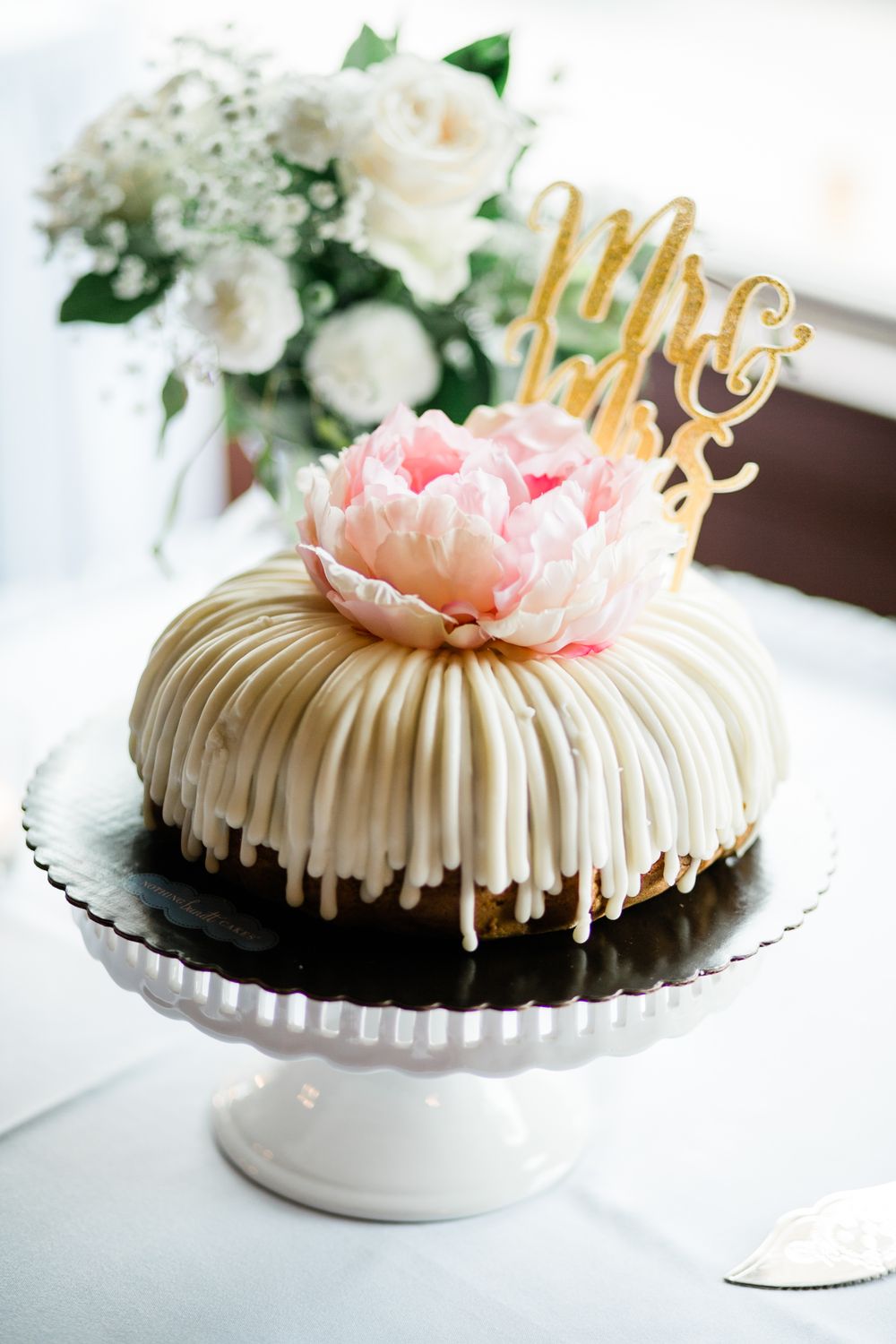 Elegant bundt wedding cake with white chocolate drizzle, pink peony, and gold Mr & Mrs topper.