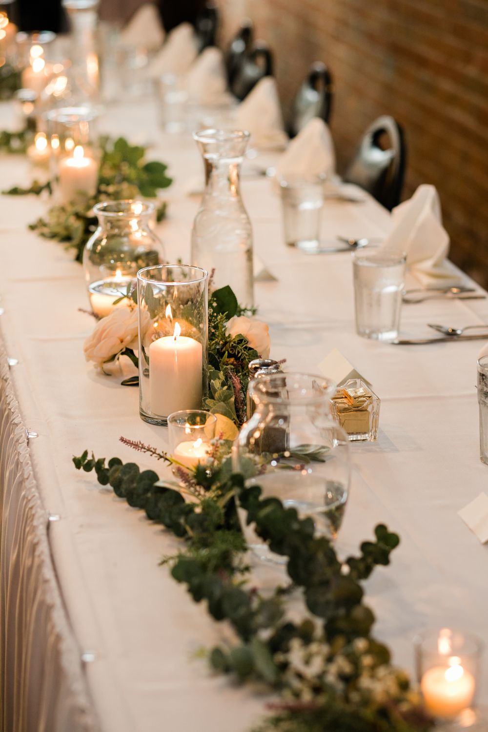 Wedding reception head table decorated with greenery garland, white candles, and floral centerpieces.