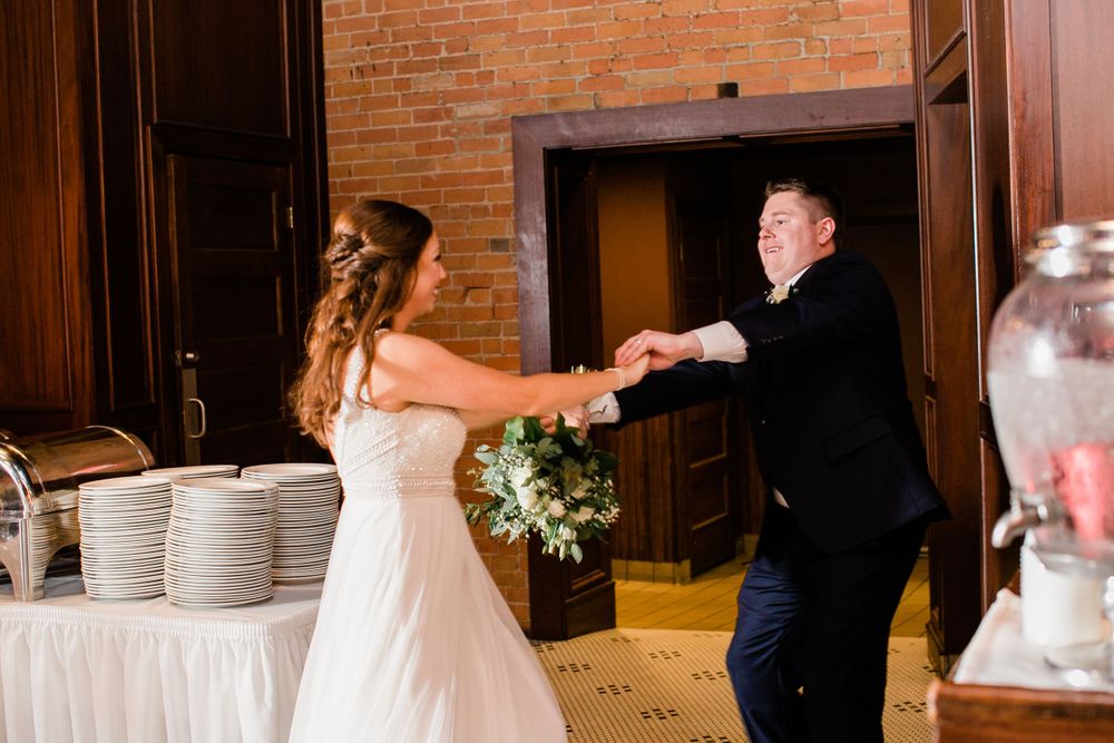 Bride and groom share a joyful dance during their wedding reception entrance holding a bouquet.