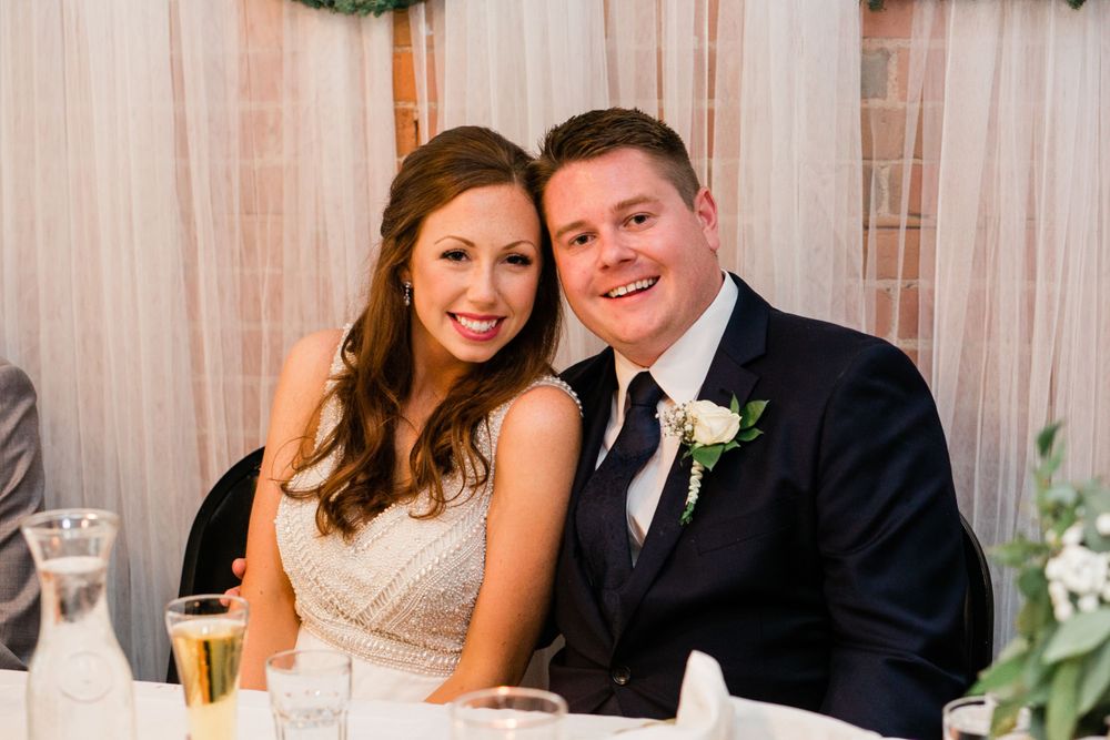 Bride and groom pose together smiling at the head table during their wedding reception.