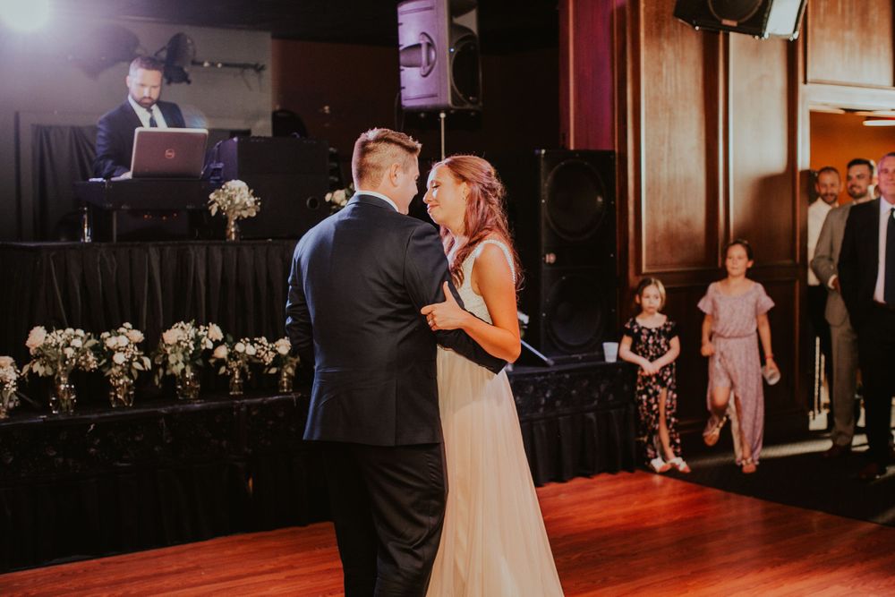 Bride and groom sharing their first dance at wedding reception with DJ in background.