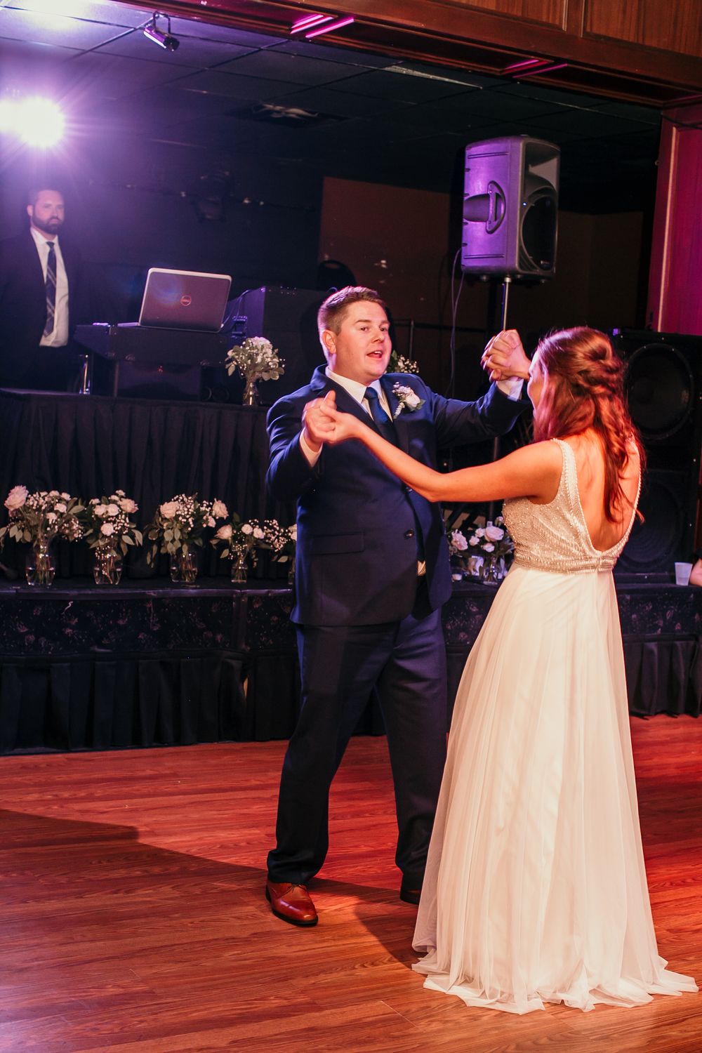 Bride and groom dancing joyfully on wedding reception dance floor with floral arrangements.