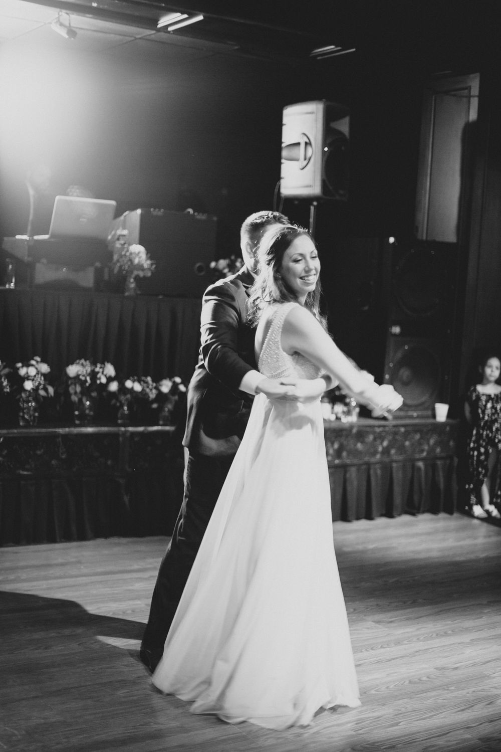 Bride and groom share their first dance in black and white wedding photo on wooden dance floor.