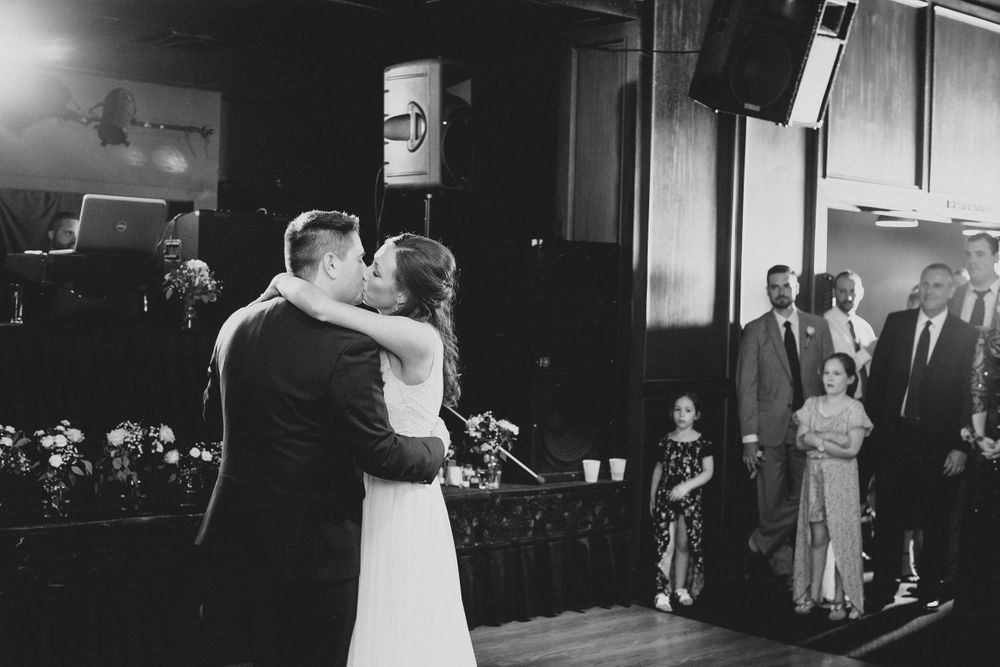 Bride and groom embrace during first dance as wedding guests watch in black and white photo.