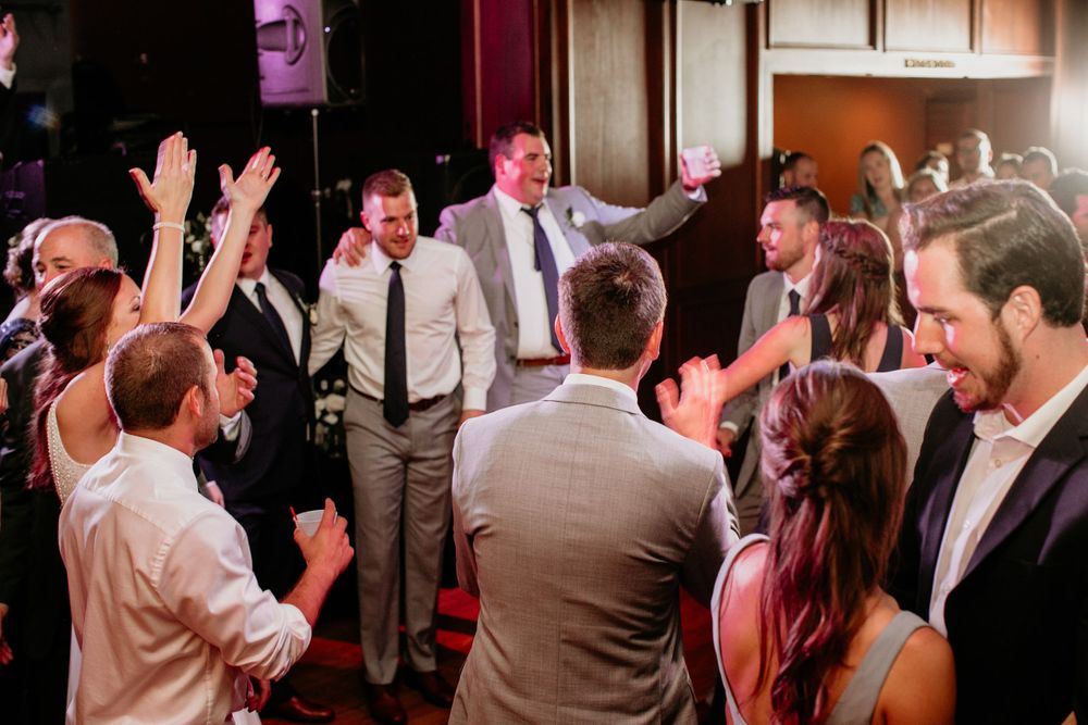 Energetic wedding guests celebrate on dance floor with raised hands at lively reception party.