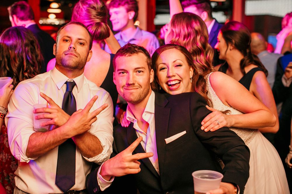 Three wedding guests pose playfully for photo on dance floor at vibrant wedding reception.