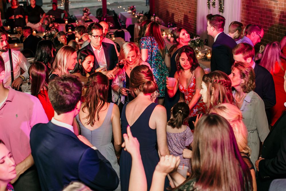 Large crowd of wedding guests mingle and celebrate at elegant dimly lit reception venue.