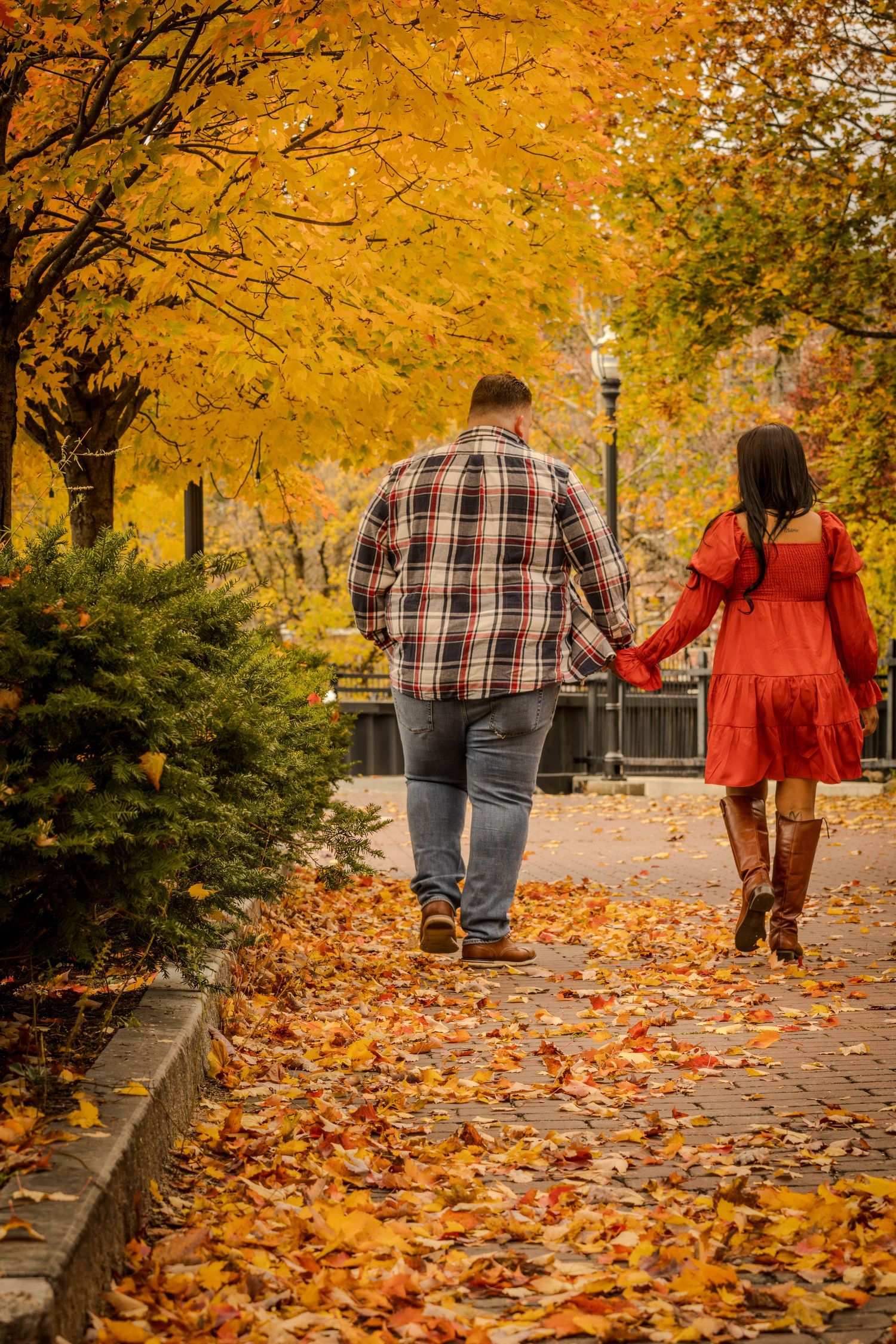 Couple holding hands while walking on autumn path covered in fallen orange leaves.