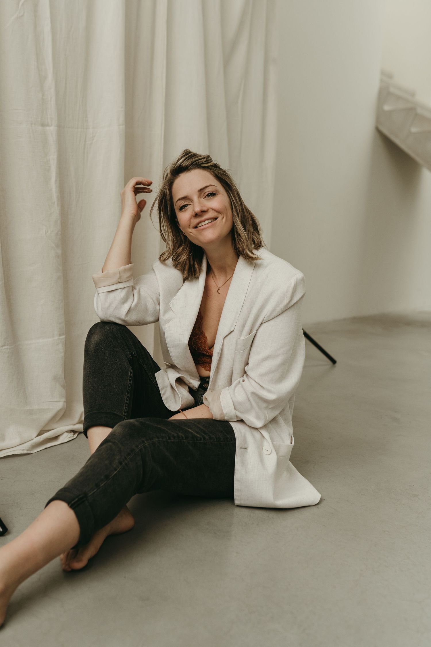 Casual portrait of someone sitting on floor wearing white blazer and dark jeans.