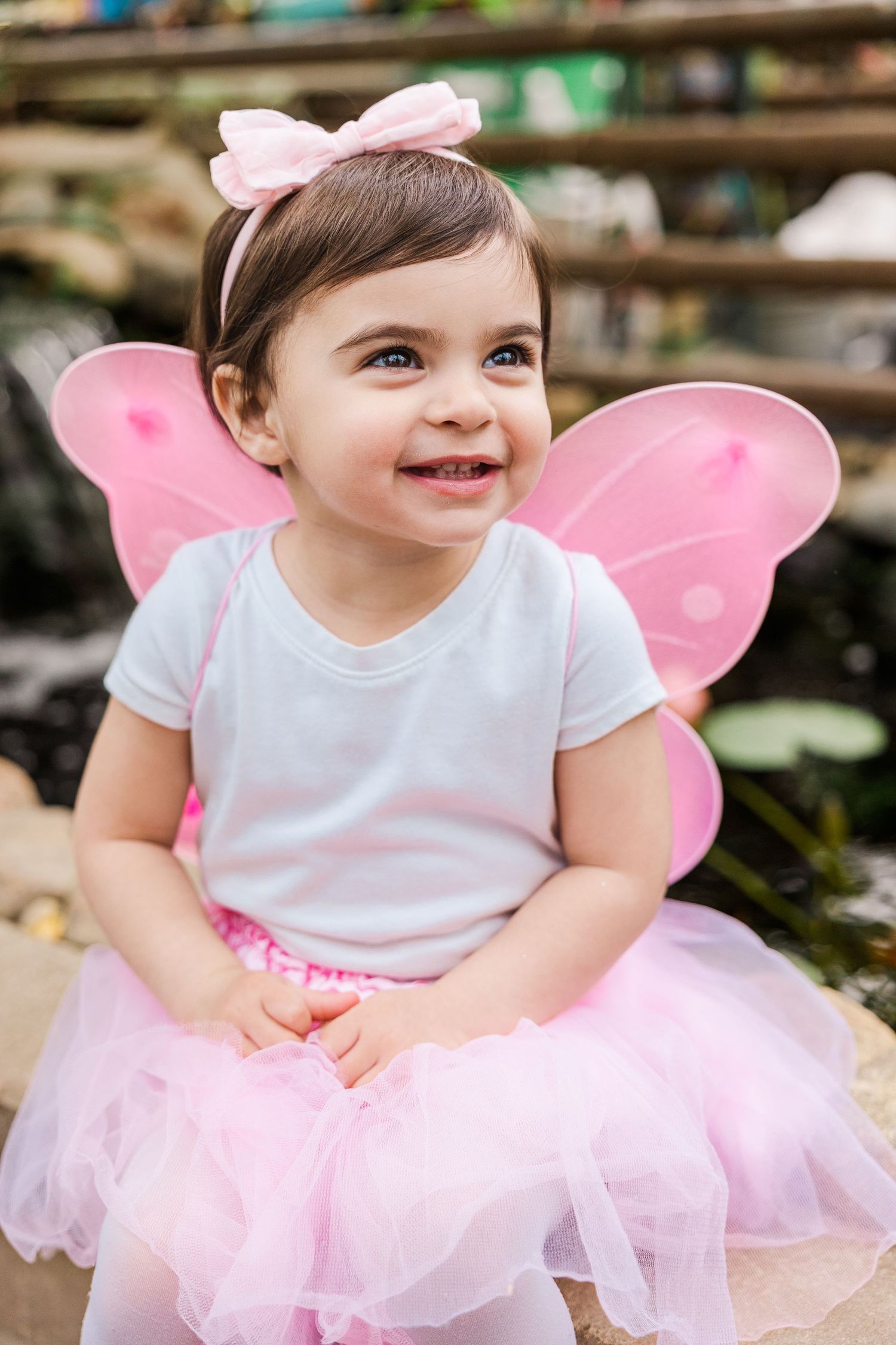 Delighted child in fairy costume with pink wings and tutu poses in garden.