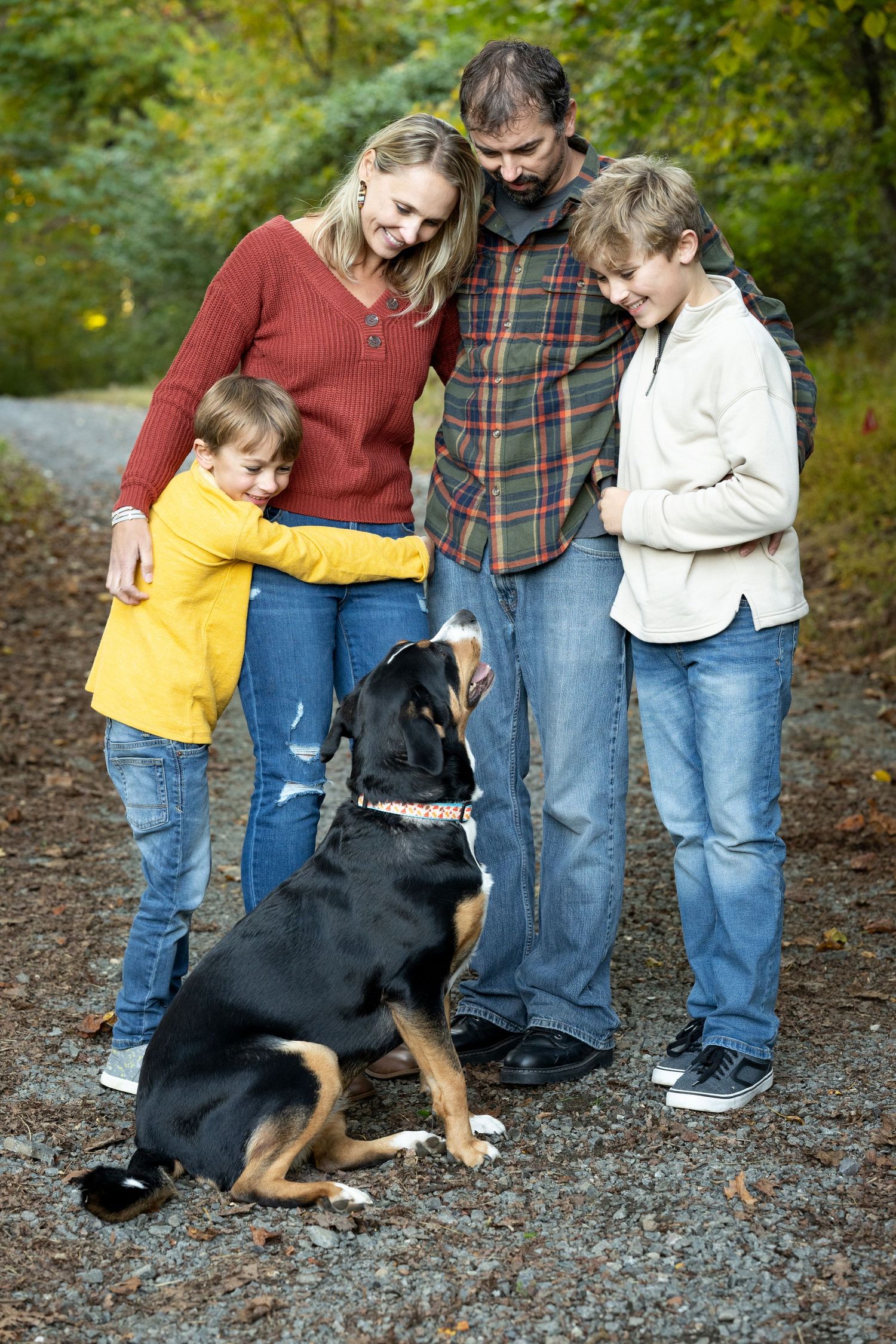 Family with two children and their black and tan dog posing on a gravel path in autumn.
