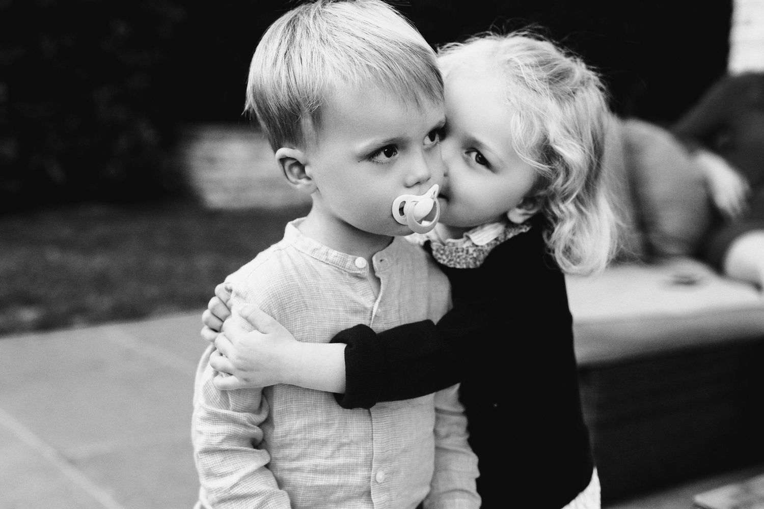 A tender black and white portrait of two children sharing an affectionate moment outdoors.
