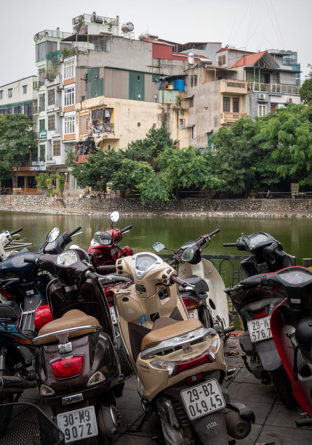 Weathered apartment buildings overlook a waterway where numerous motorcycles are parked along the bank.
