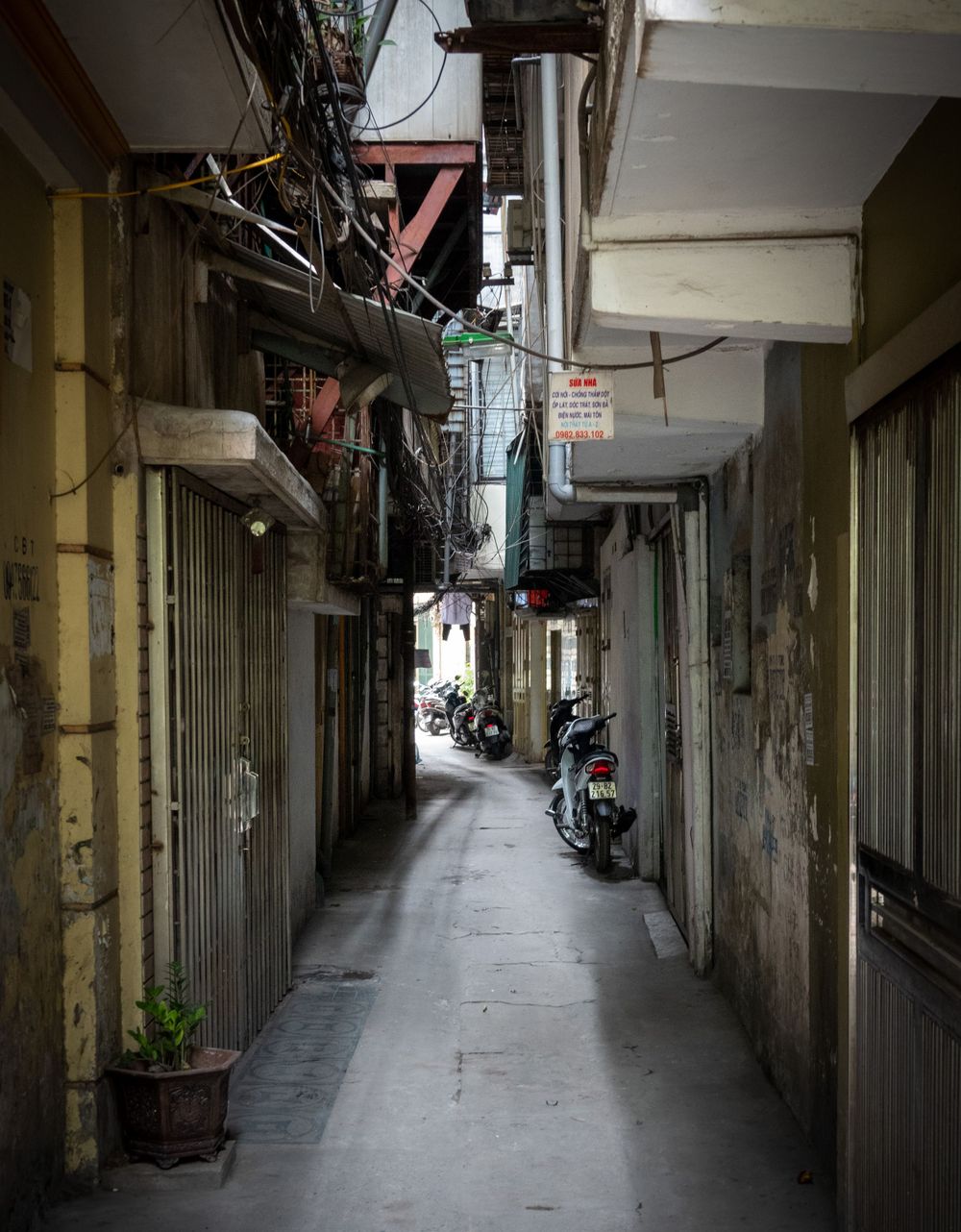 Narrow urban alley with old buildings and exposed utilities showing typical Asian architecture.