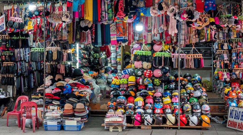 Colorful retail display showing stacks of helmets, clothing and accessories for sale in a Vietnamese market.