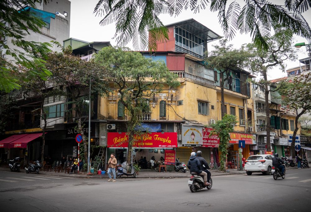 Colorful corner building with storefronts and motorcycles on a busy Vietnamese street.