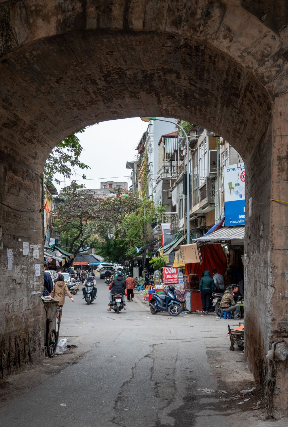 View through stone archway of busy street with motorcycles and shops in Vietnam.