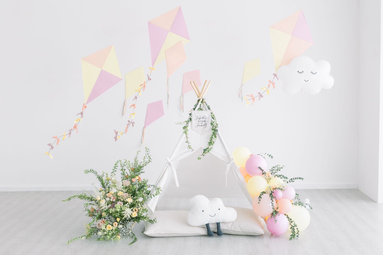 Dreamy party decoration with pastel kites, flowers and white cloud elements against white wall.