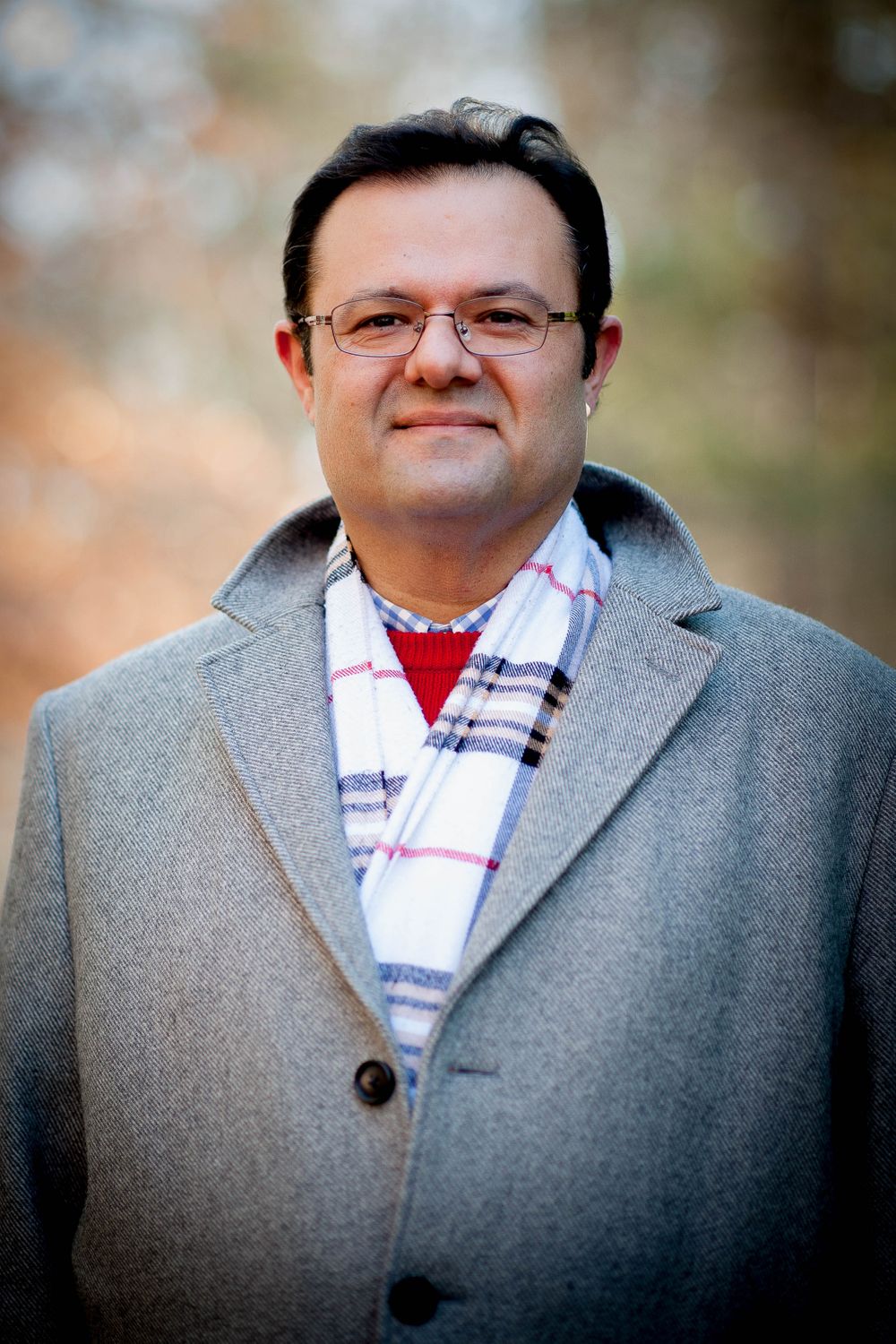 Man is an overcoat, wearing glasses and posed for headshots.
