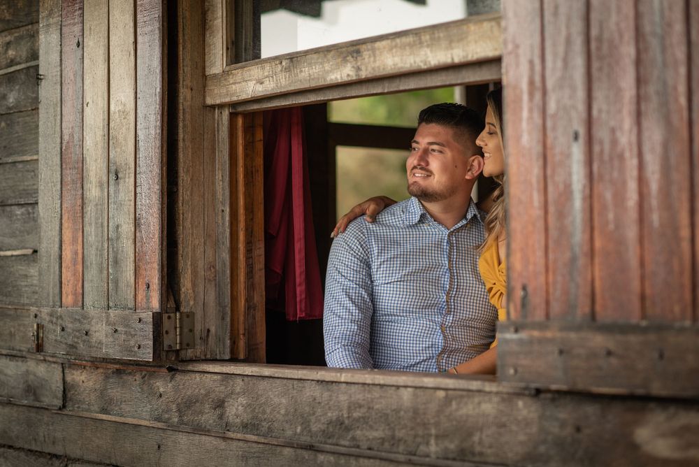 Person looking thoughtfully through rustic wooden window frame in natural lighting.