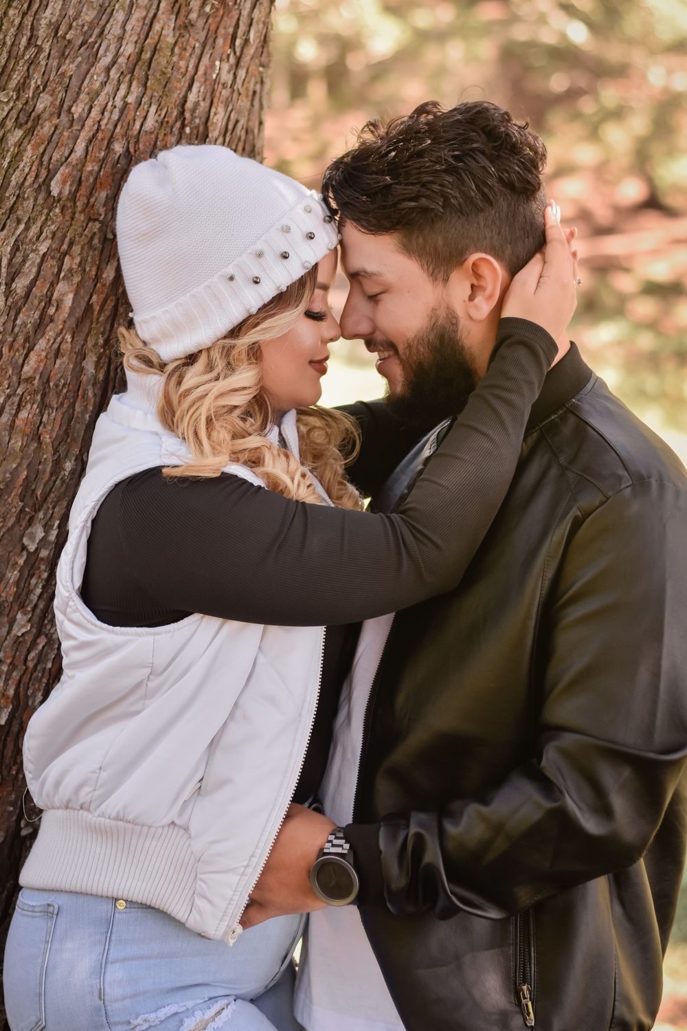 A tender winter moment shared between a couple against a tree trunk in a wooded setting.