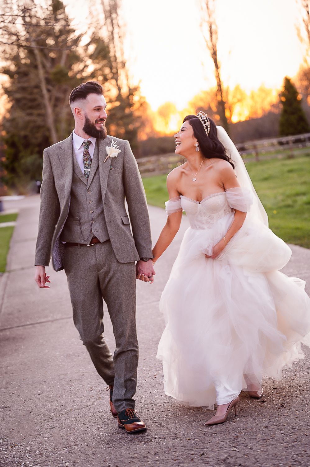 A couple walks hand in hand along a path at sunset, the bride's dress flowing in motion.