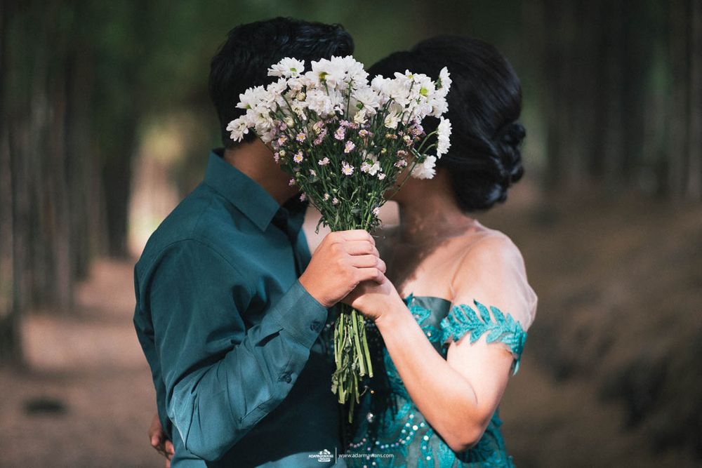 A romantic couple hidden behind a bouquet of white baby's breath flowers in a forest setting.