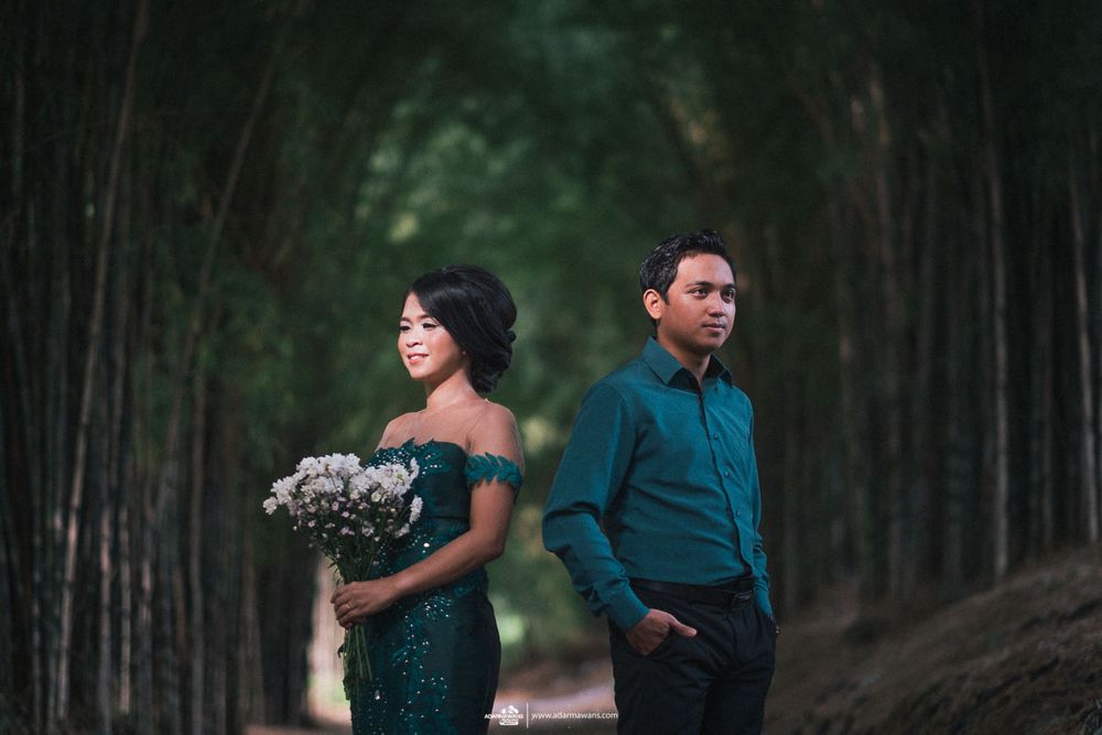 A couple in formal attire posing separately in a tree-lined forest path.