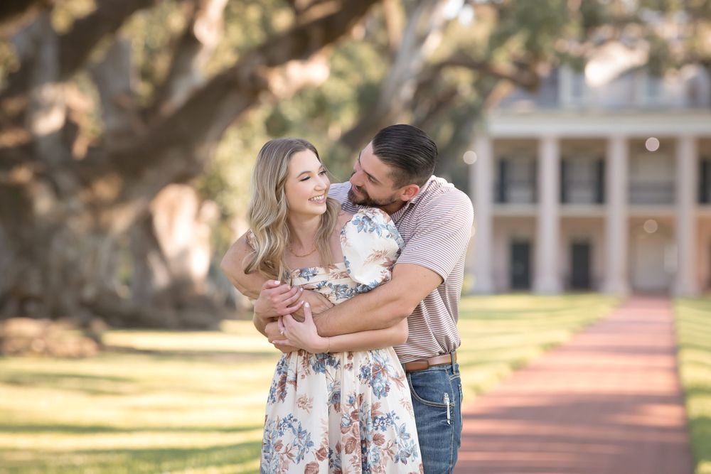 A couple shares intimate moments on a brick pathway with a southern plantation-style building backdrop.