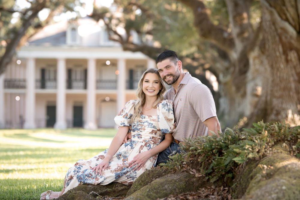 Romantic outdoor photoshoot with oak trees and white colonial architecture in the background.