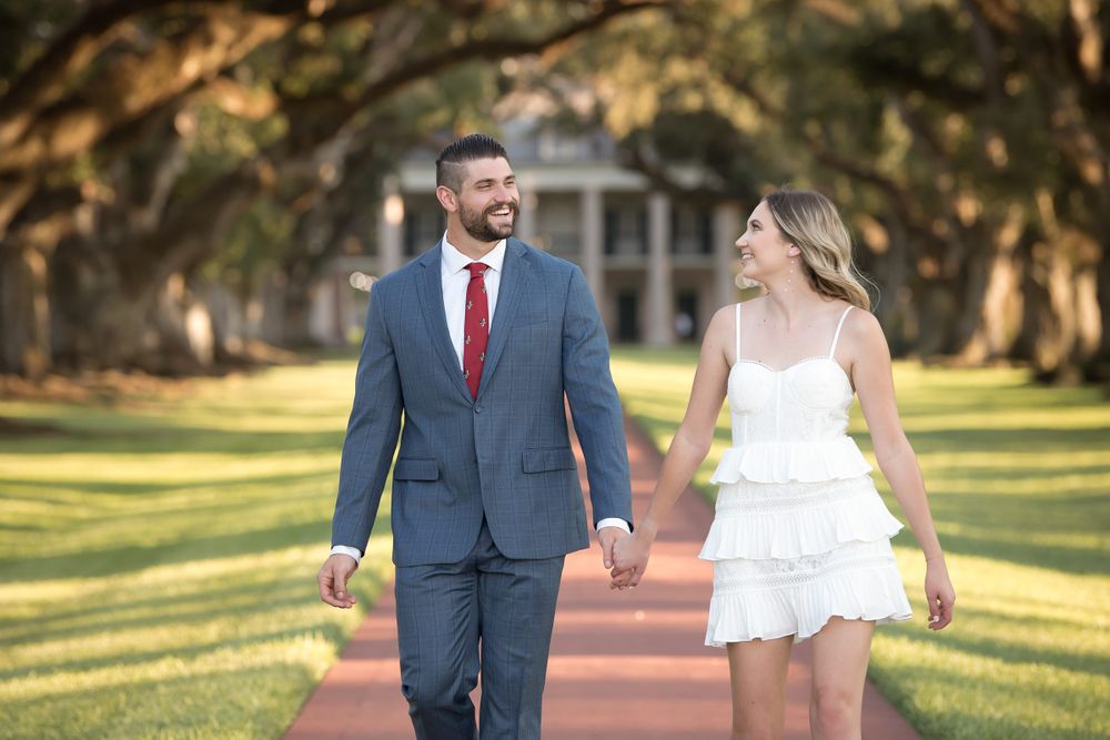 Romantic couple poses together on a tree-lined pathway during golden hour engagement photo session.