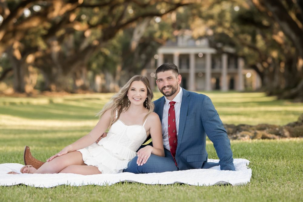 Couple relaxes on white blanket during outdoor engagement session near historic building.