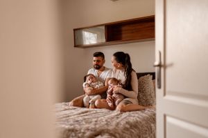 View through doorway of parents with twin babies sitting on bed.