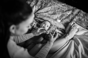 Black and white intimate portrait of parent playing with baby on bed.