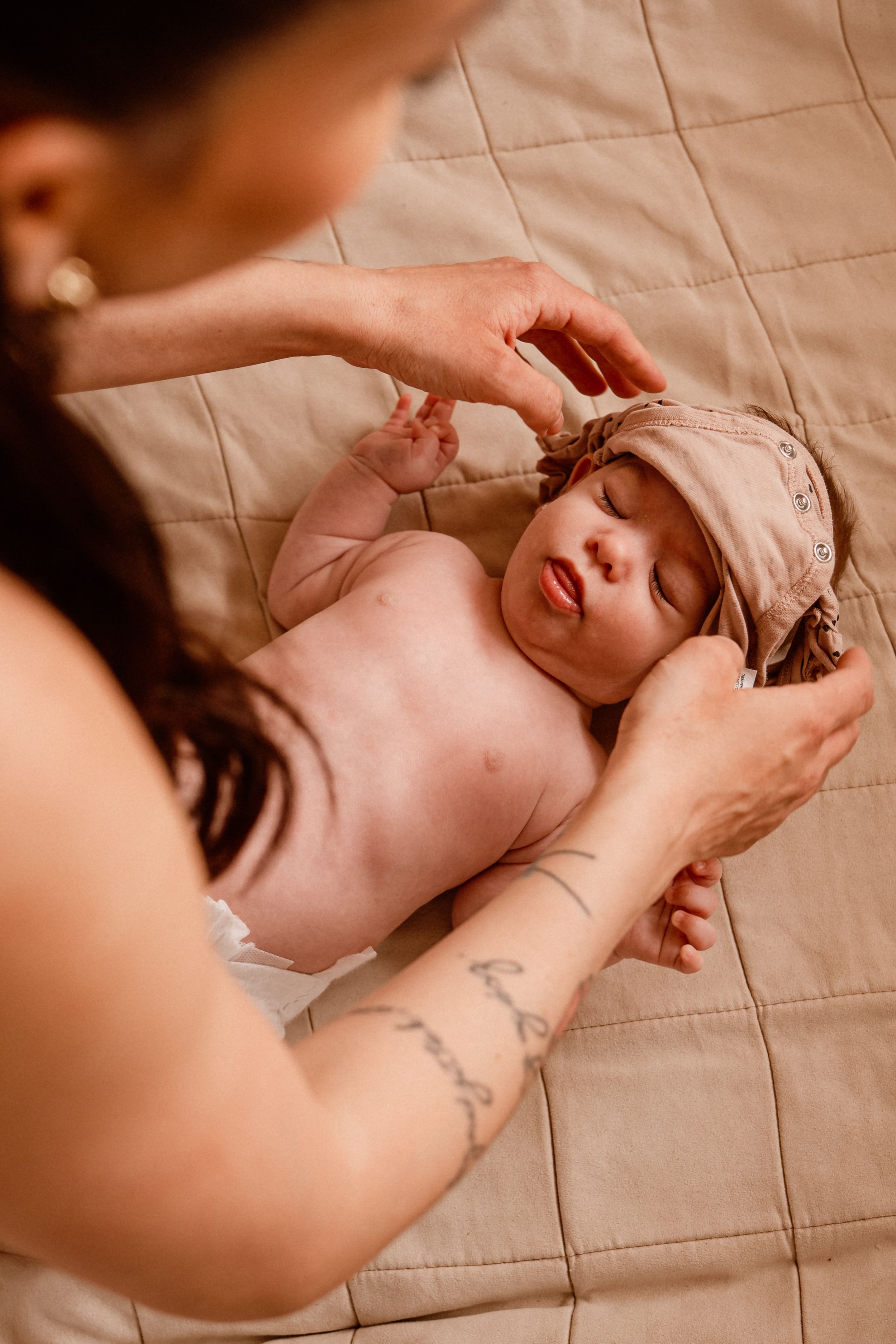 Gentle hands caring for peaceful sleeping baby on quilted bedding.