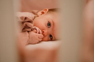 Close-up of baby in pink clothing lying on cream bedding.