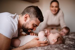 Parent playfully interacting with baby lying on bed.