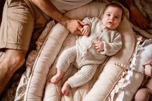 Overhead view of a baby in ribbed knitwear resting on a plush white lounger.