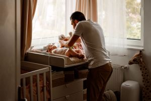 Parent changing baby's diaper at wooden changing table near window.