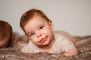 Close-up of smiling baby with rosy cheeks on textured blanket.