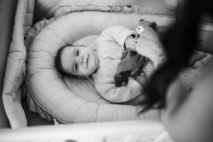 Baby lying in grey lounger cushion smiling while wearing knit sweater.