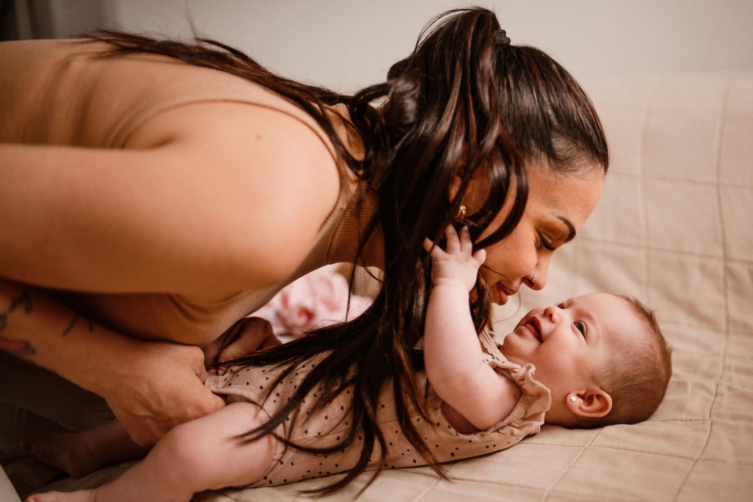 Joyful intimate moment between parent and baby on beige bedding.