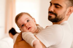 Baby in white onesie being held against warm background.