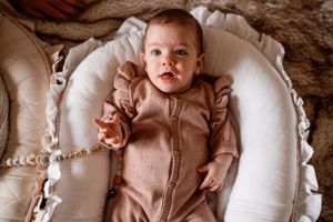 Baby wearing a pink onesie lies contentedly in a white cushioned baby lounger.