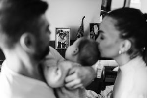 Black and white intimate family moment showing parents interacting with their baby in a tender embrace.