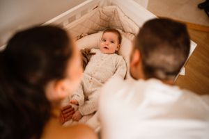 Parents gazing down at their baby lying in white crib.