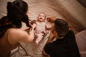 Parents share a joyful moment with their laughing baby on a bed.