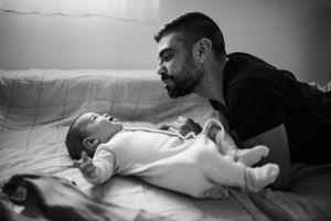A tender black and white moment between parent and baby lying on bedding.
