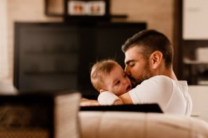 Tender moment between parent and infant on couch in warm lighting.