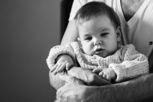 Black and white portrait of a baby in a knit sweater being held protectively.